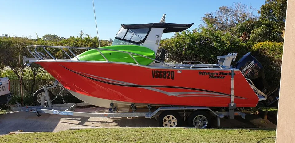 Red cabin boat on a trailer with a green kayak on the foredeck