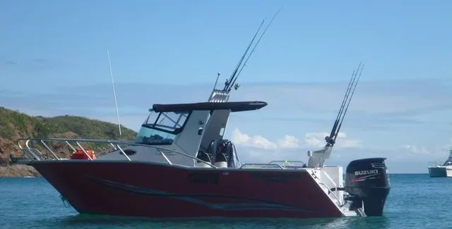 Red hardtop fishing boat with rods raised while resting on the water