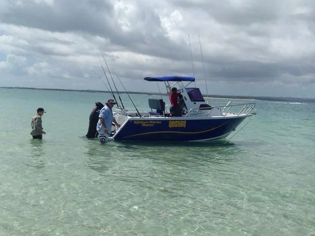 People standing in shallow water beside a blue soft top boat