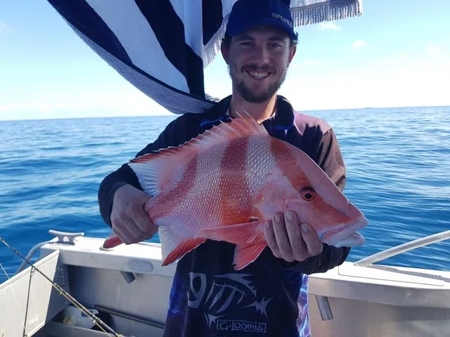 Angler holding a red-and-silver fish beneath a striped shade cover