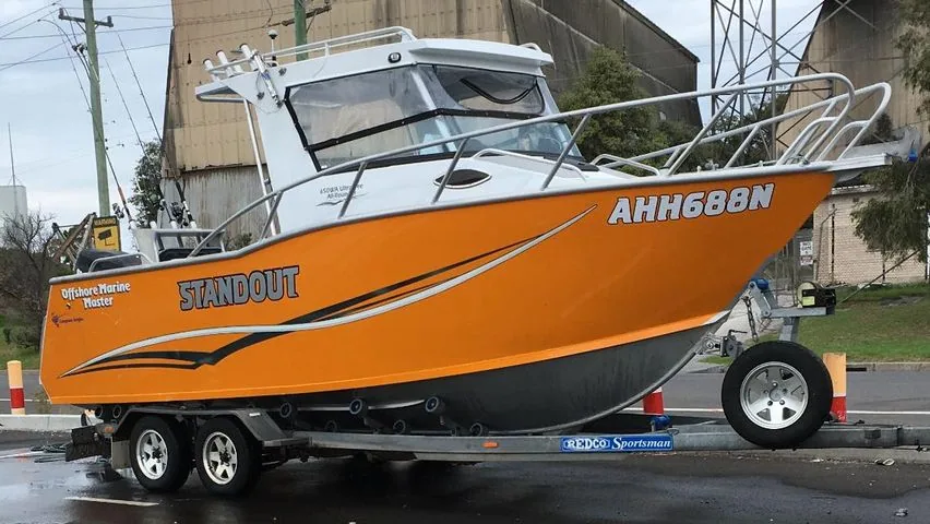 Orange hardtop boat with Standout hull lettering on a trailer
