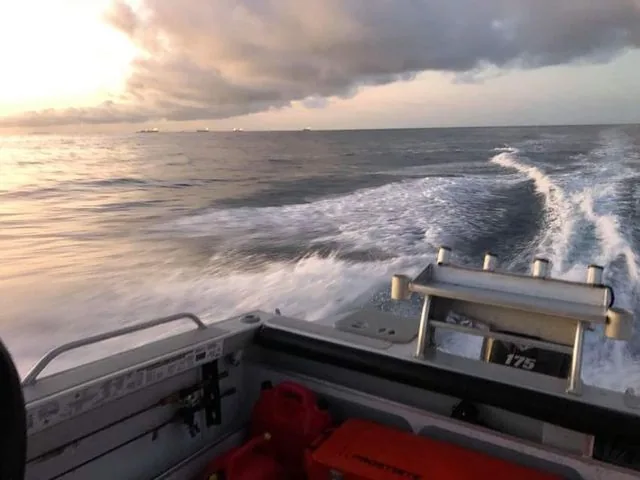 View over a boat transom and foamy wake beneath a cloudy sunset
