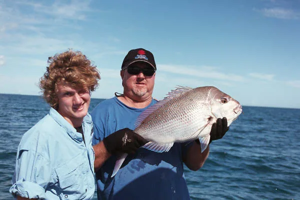 Two anglers holding a large silver fish against the open-water backdrop