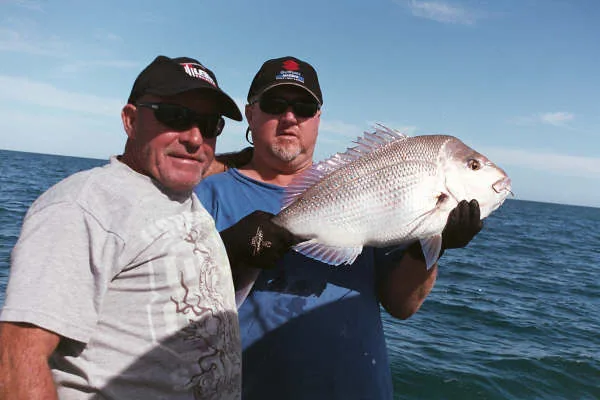 Two anglers posing with a large silver fish aboard a boat