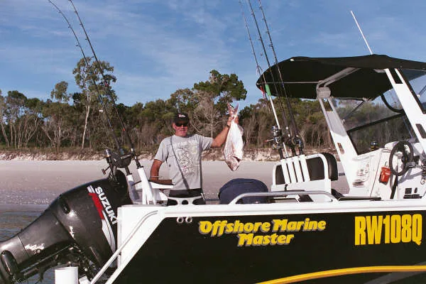 Angler holding a fish aboard a black OMM boat near the beach