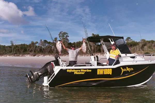 Angler raising two fish aboard a black-and-yellow boat in shallow water