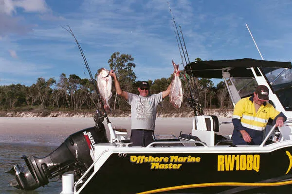 Close view of an angler holding two fish above the rear deck