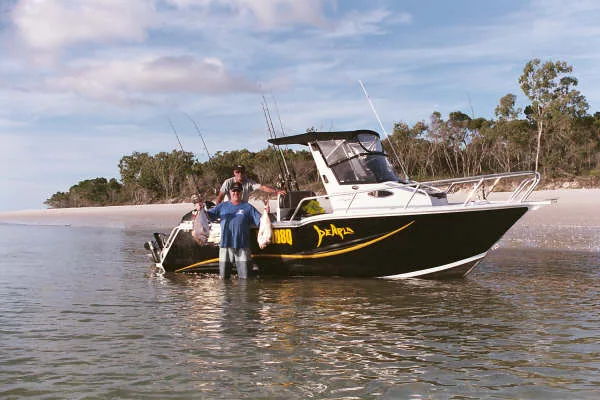 Angler standing in shallow water beside a black cabin boat