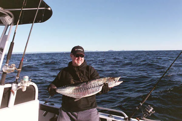 Angler holding a long silver fish on the rear deck