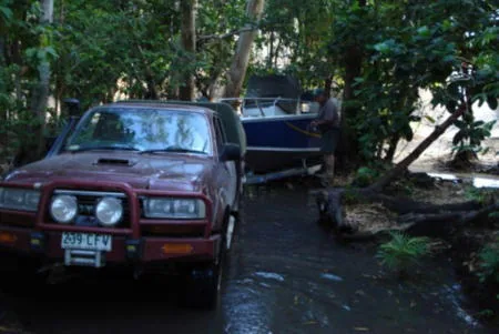 Red four-wheel-drive vehicle towing a boat along a wooded track