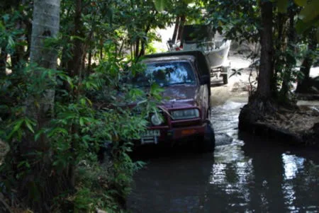 Red four-wheel-drive vehicle and boat trailer on a water-covered wooded track