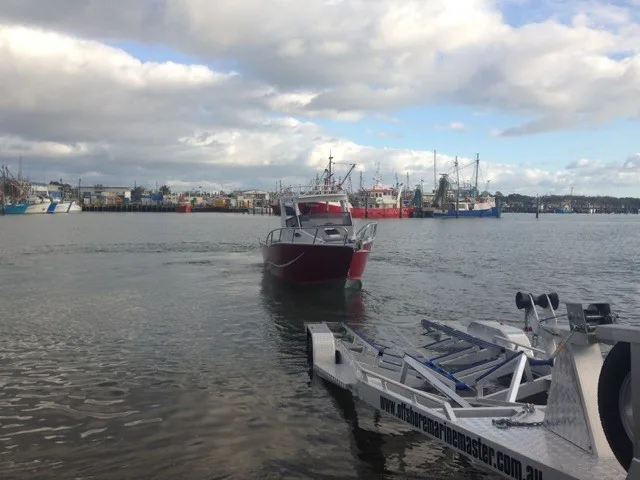 Boat trailer at a ramp with a red boat in the water beyond